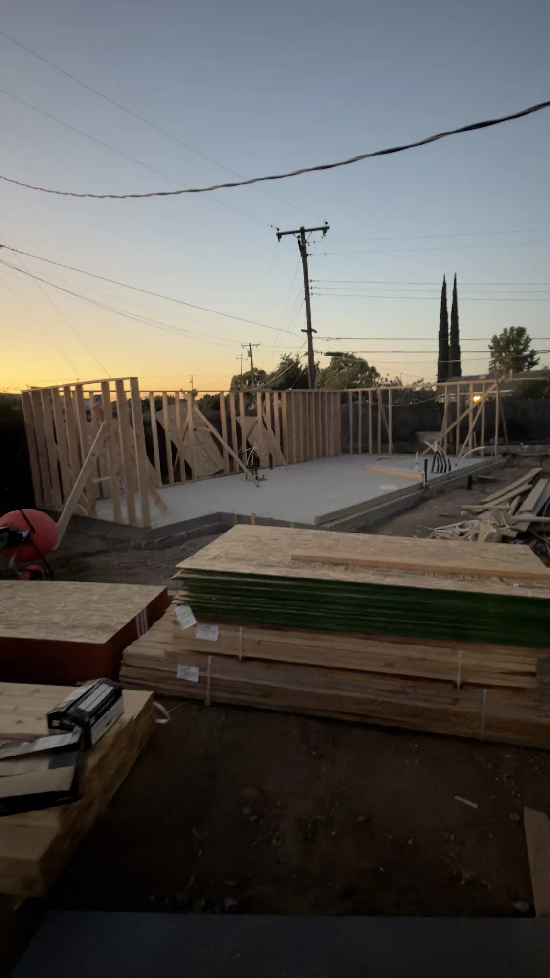 ADU wall framing at dusk with lumber and sheathing staged on the slab