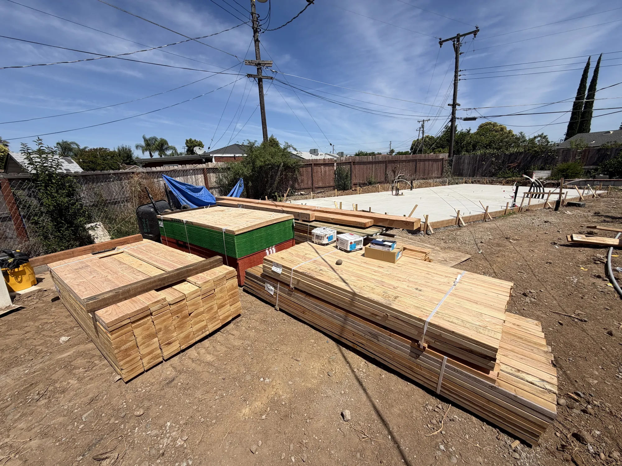 Framing lumber and sheathing staged beside a cured ADU slab on a Sacramento-region job site