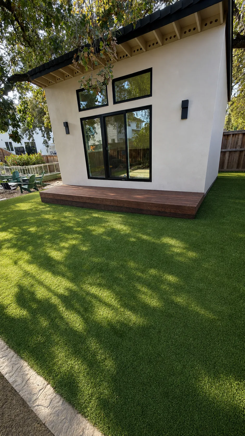 Completed detached ADU with white stucco, black-framed windows, a wood deck landing, and finished landscaping, built by Folsom City Carpentry