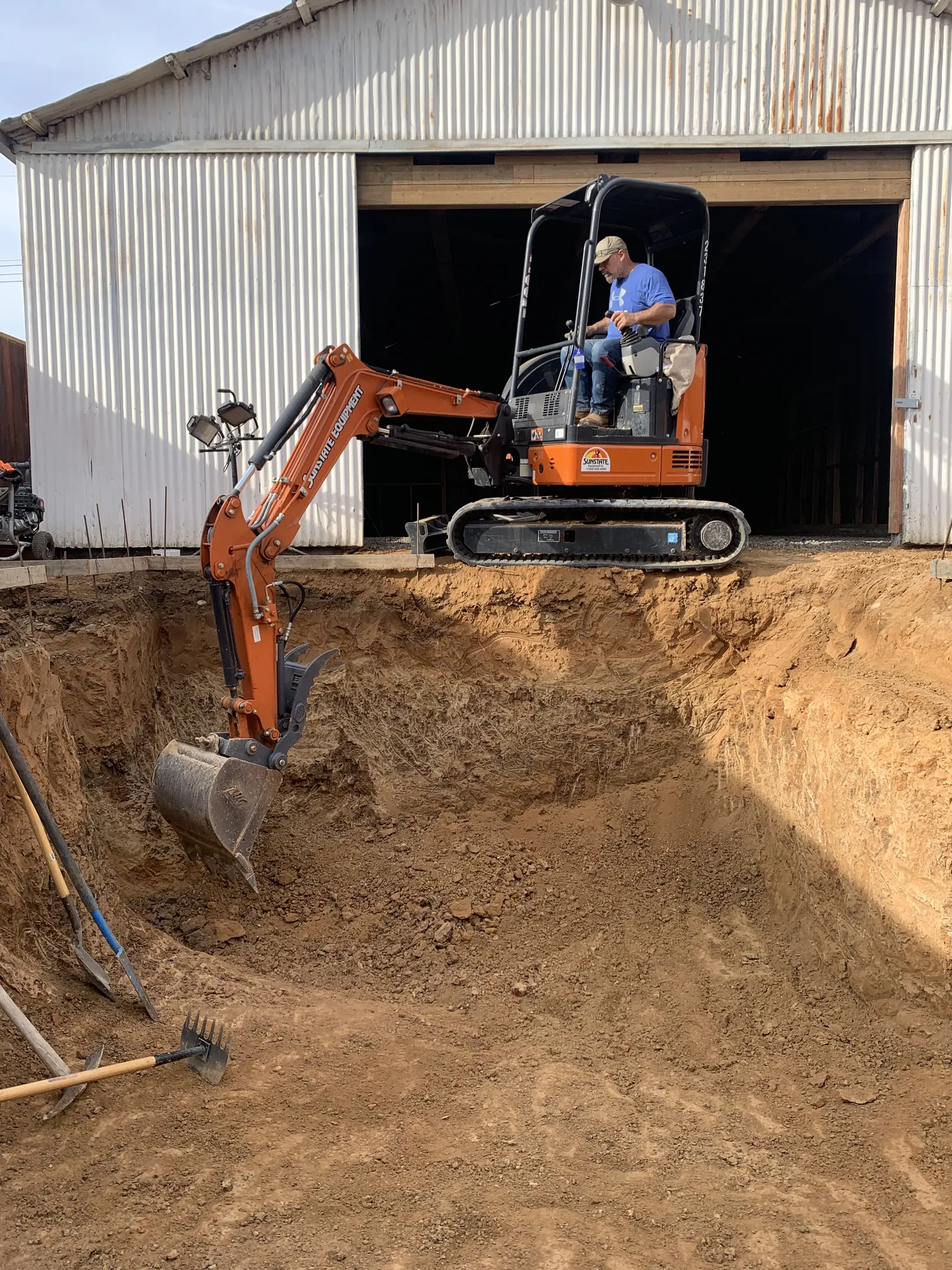 Mini excavator digging the pool excavation alongside the metal hangar building