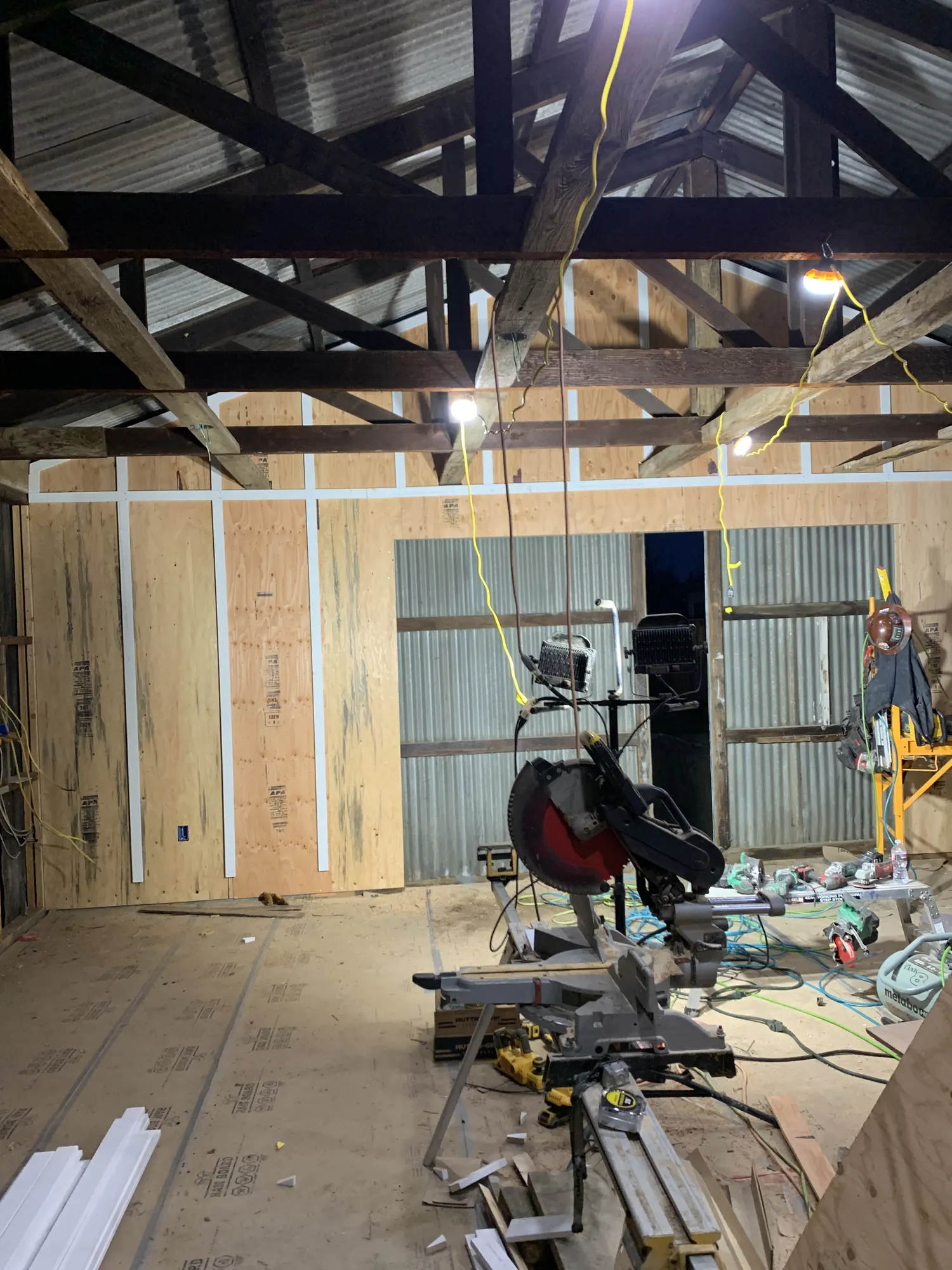 Hangar interior with walls sheathed and carpentry underway under work lights at night