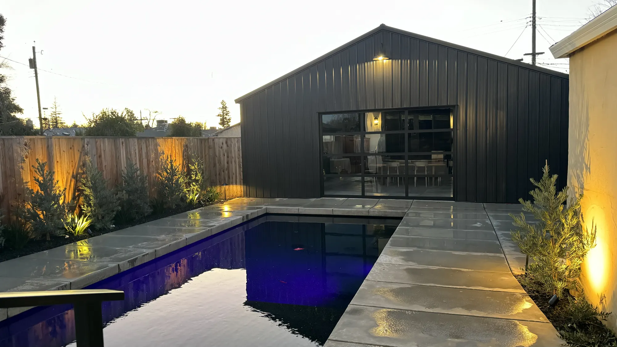 Converted airplane hangar residence near Marysville, California at dusk, showing the finished pool, decking, and glass garage door