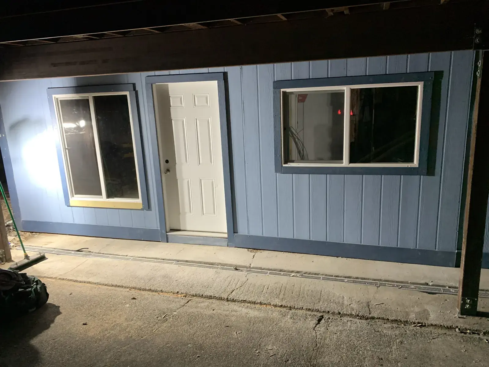 The finished ADU exterior at night, clad in blue board-and-batten with a new white entry door and windows