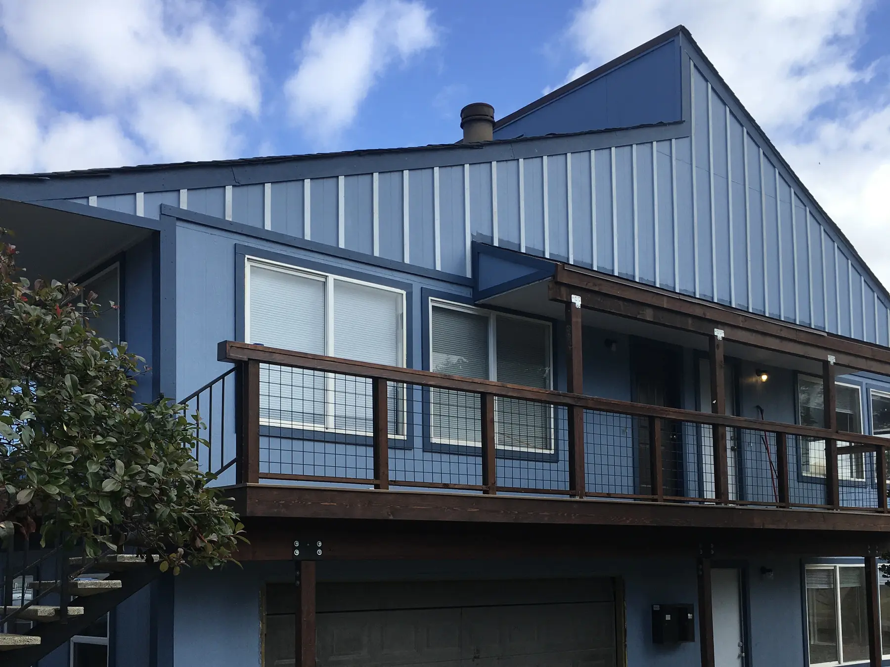 The finished four-unit apartment building in Arcata from the street: light blue Hardie board-and-batten, rebuilt second-floor deck with cedar rails and welded wire infill, garage below