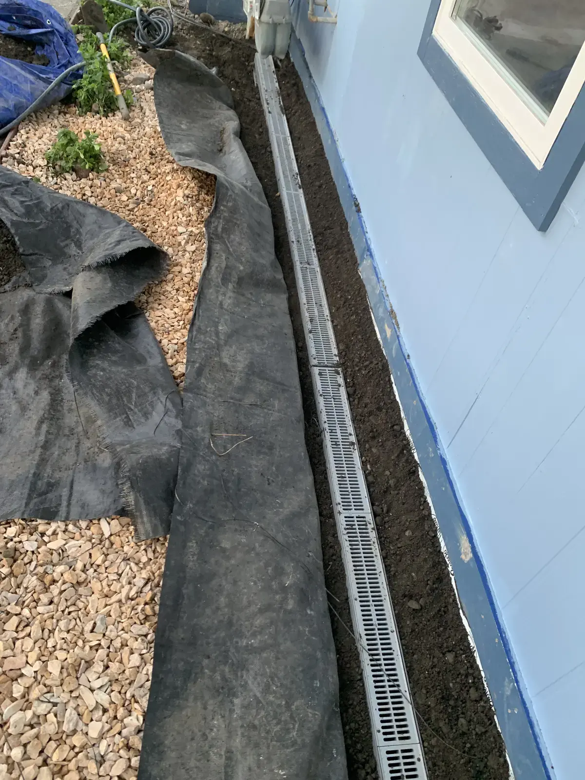 Finished channel drain set in drain rock against the completed blue siding