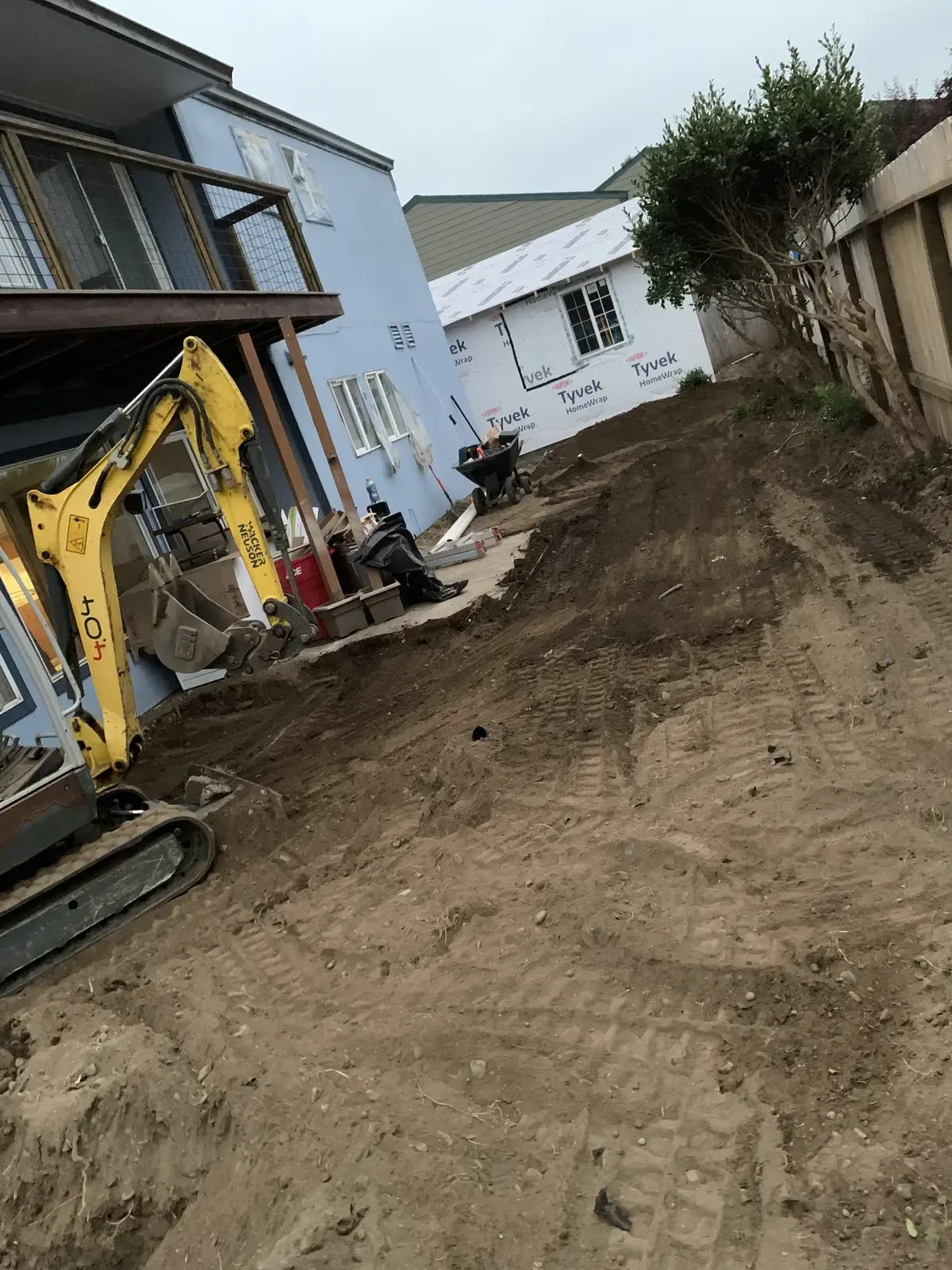 Mini excavator digging a drainage trench tight against the apartment building