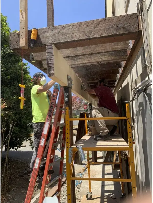 Worker in a dust mask on staging, sanding the underside of the new glulam beam before staining