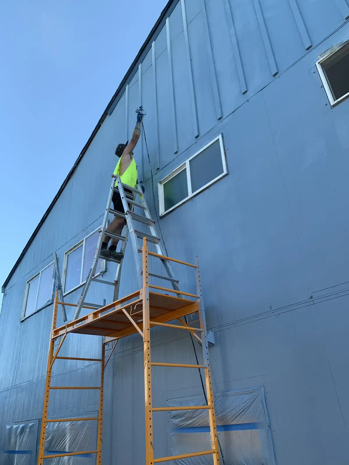 Crew member on scaffolding painting the tall gable elevation of the apartment building