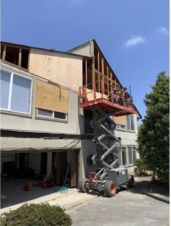 Scissor lift parked at the building with fresh plywood sheathing patches visible against the old siding