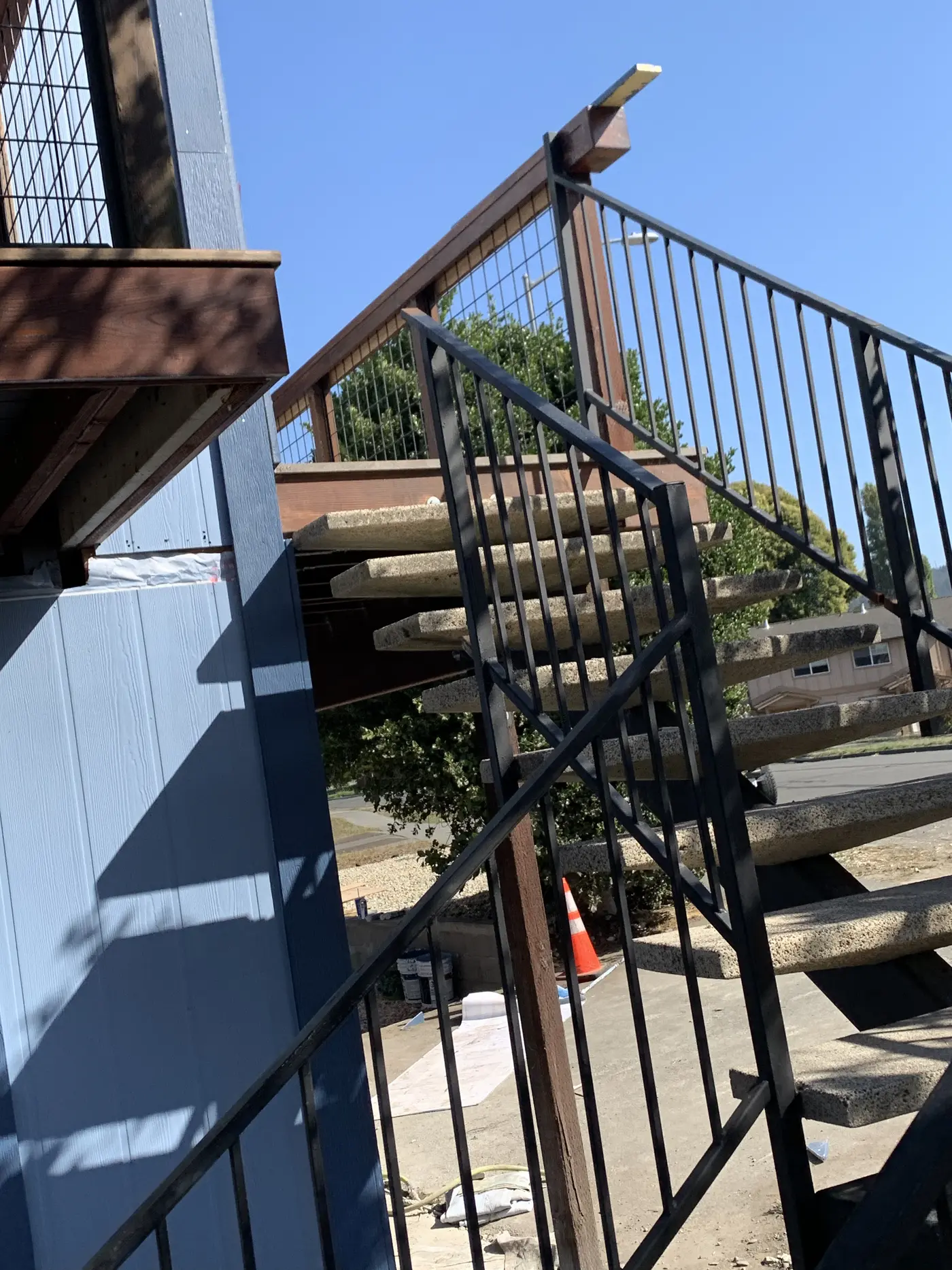 Exterior staircase with steel railing running beneath the rebuilt deck, new blue siding alongside