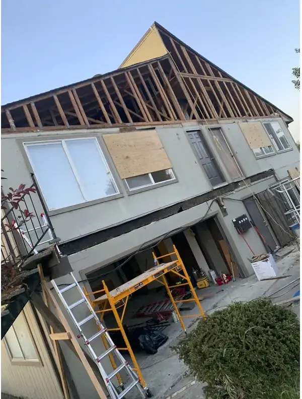 The building with all siding removed, roof structure and wall framing exposed