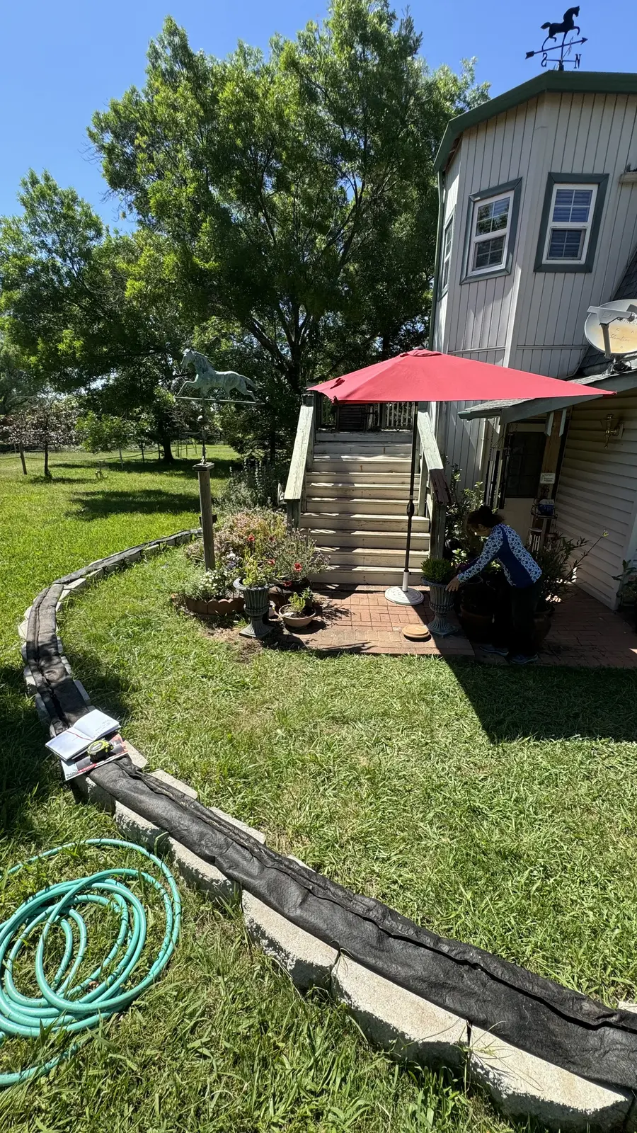 Stacked concrete blocks with black plastic sheeting behind them forming a makeshift flood barrier along the lawn edge
