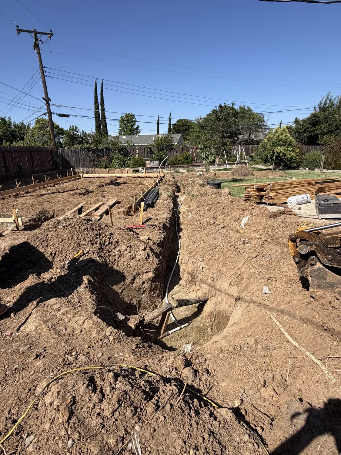 Excavation and utility trenching for a detached ADU foundation, trench and conduit open in a Sacramento backyard