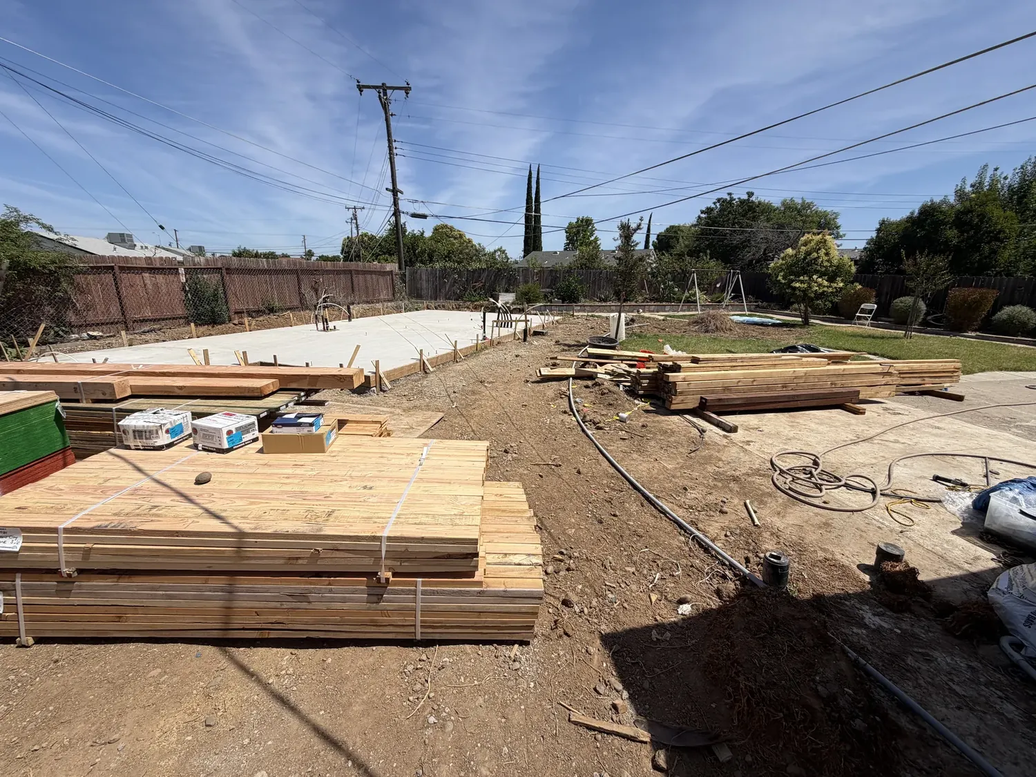 Poured ADU foundation slab with edge forms and rebar dowels, framing lumber delivered alongside